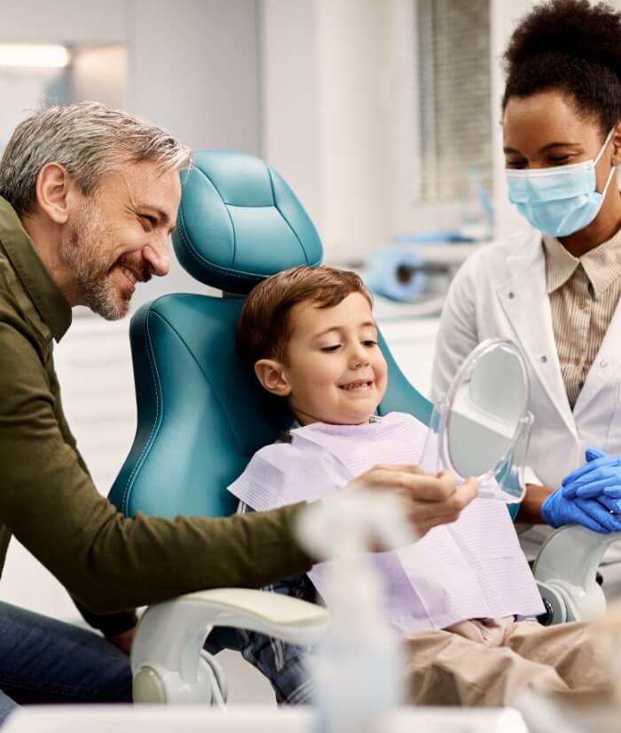 Dentist patient and parent looking at child's smile in mirror during children's dentistry visit