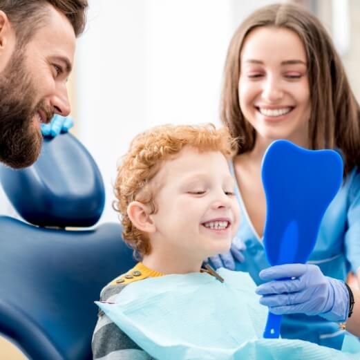 Dental team member parent and child looking at smile during pediatric dentistry visit