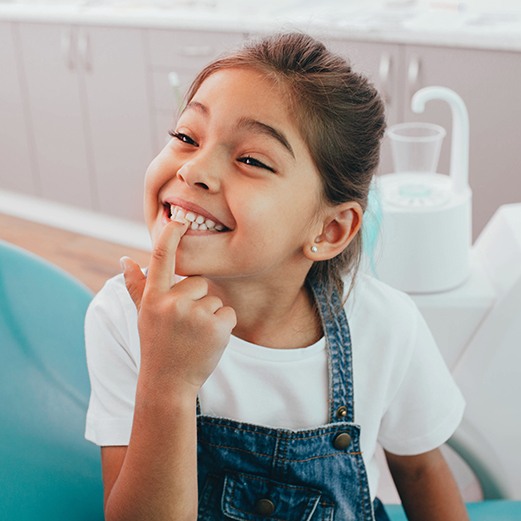 child smiling while pointing to teeth 